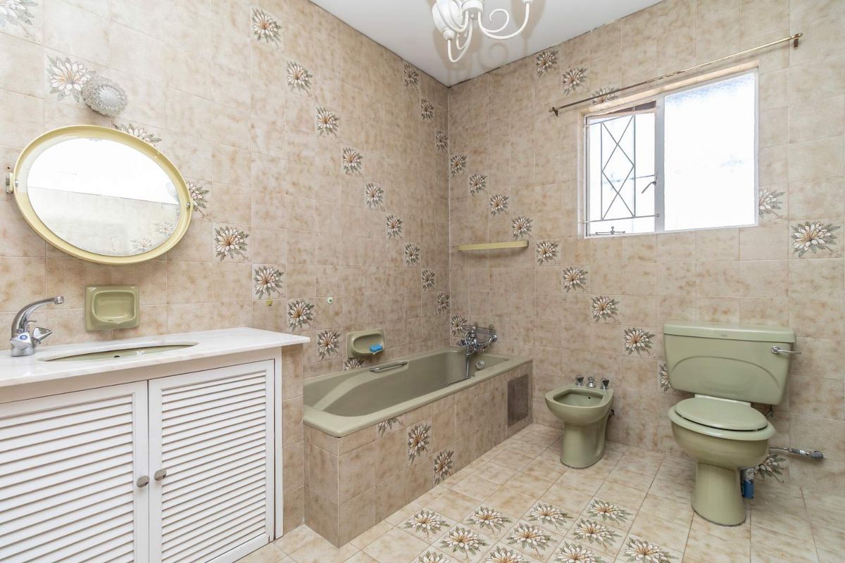 A spacious bathroom featuring a built-in vanity, bathtub, bidet, and toilet, finished with dated floral-patterned ceramic wall and floor tiles.