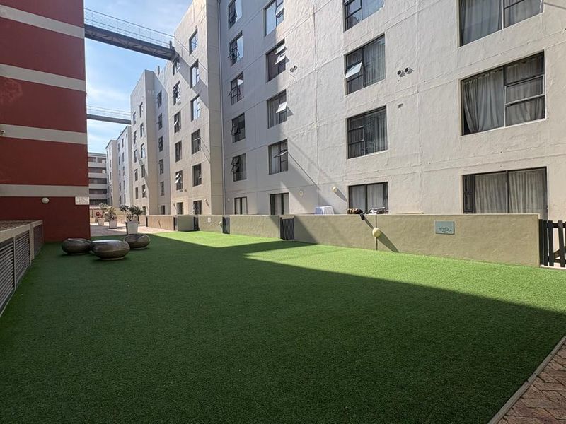 A communal outdoor terrace area featuring artificial turf, low boundary walls, and paved access between apartment building blocks.