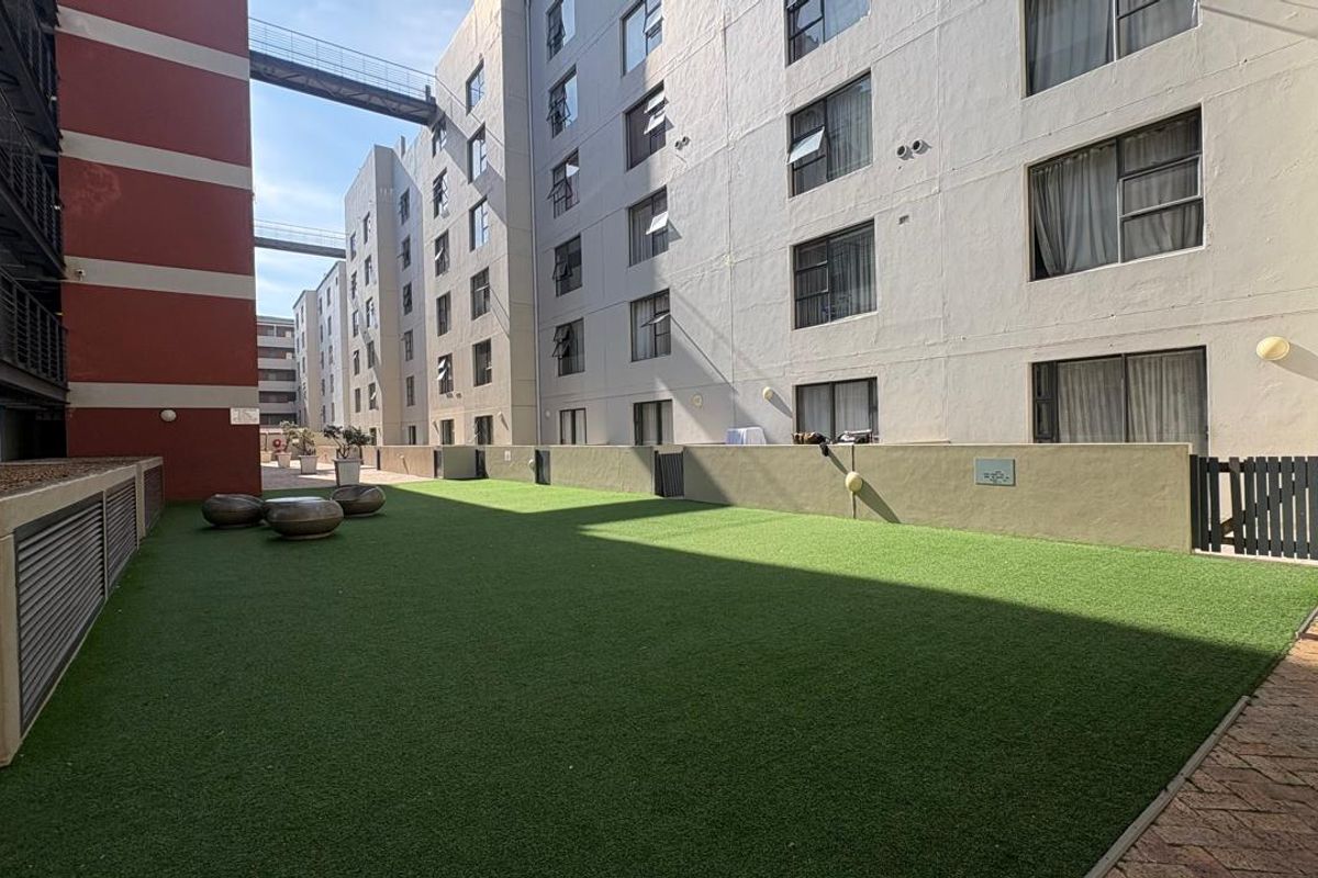 A communal outdoor terrace area featuring artificial turf, low boundary walls, and paved access between apartment building blocks.