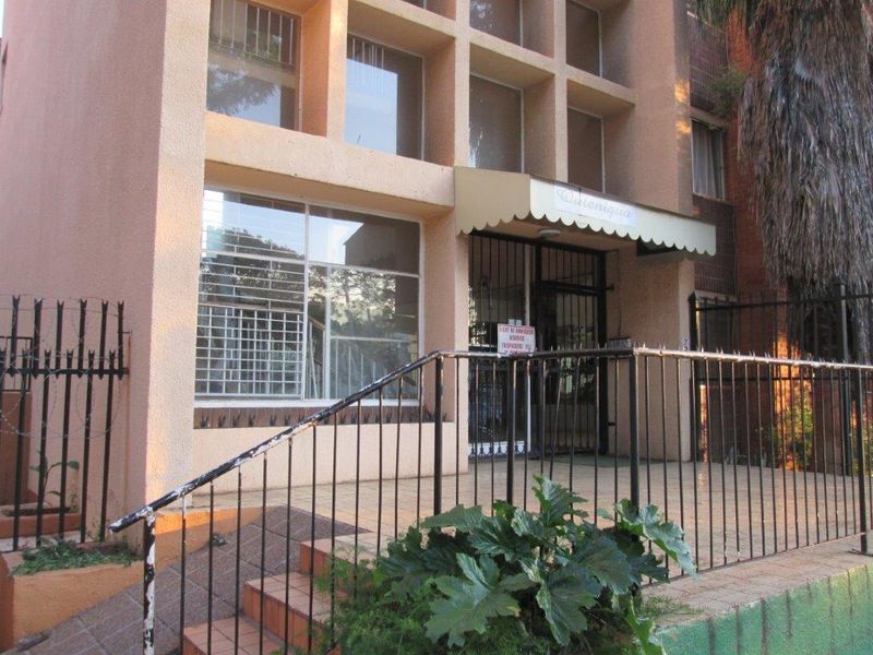 Front entrance of the apartment building featuring a security gate, metal railings, and a covered walkway with tiled steps.