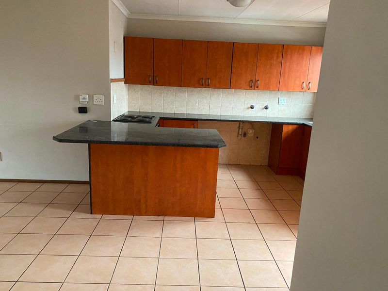 A functional kitchen featuring wooden cabinetry, granite countertops, a built-in electric hob, and tiled flooring, currently vacant and ready for updates.