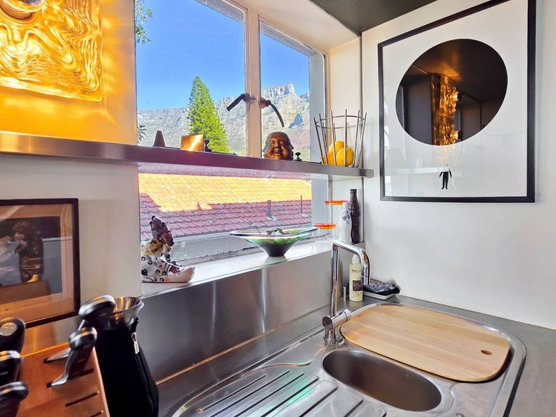 A modern kitchen area featuring a stainless steel countertop, integrated sink, and a large window offering scenic mountain views.