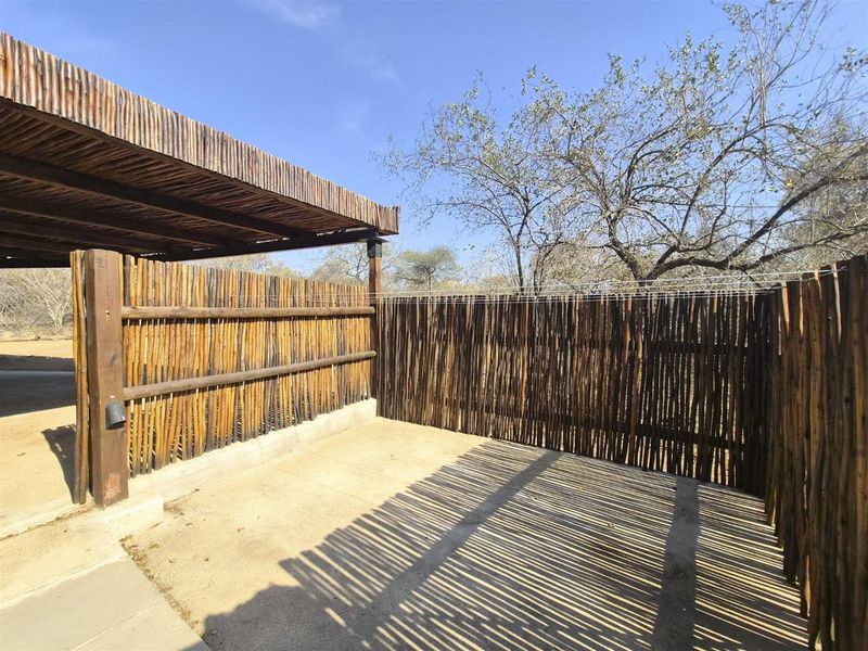 An outdoor patio area featuring a thatched roof structure and rustic timber pole fencing, providing a shaded space for outdoor relaxation.