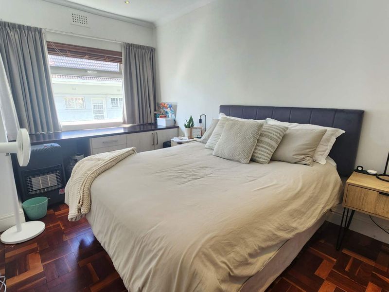 A cozy bedroom featuring classic parquet flooring, built-in window cabinetry, and neutral wall finishes, providing a functional and comfortable sleeping space.