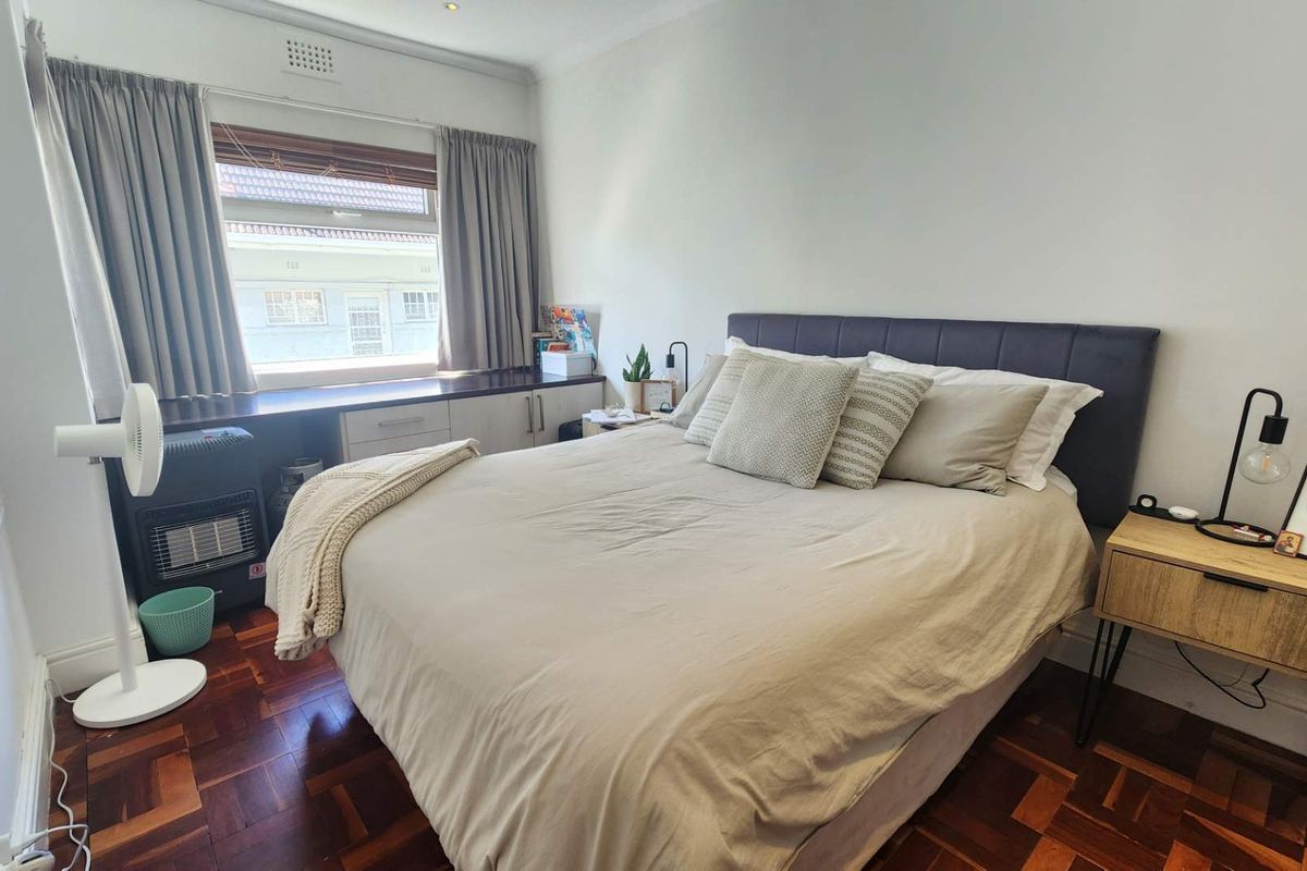 A cozy bedroom featuring classic parquet flooring, built-in window cabinetry, and neutral wall finishes, providing a functional and comfortable sleeping space.