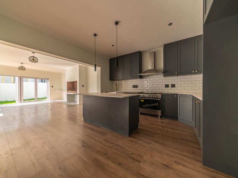 Modern open-plan kitchen and living area featuring dark cabinetry, a central island, subway tile backsplash, and seamless access to the outdoor space.