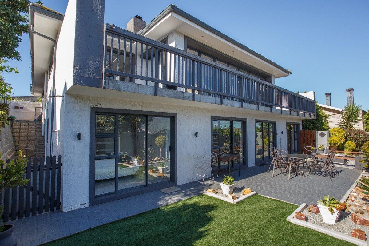 Rear view of the property featuring a paved patio, artificial lawn, and a spacious upper-level balcony with sliding door access to the interior.