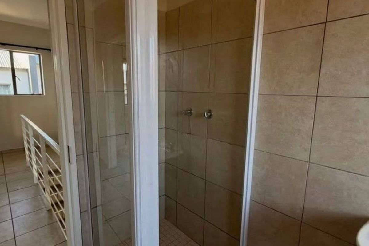 A bathroom featuring a corner shower enclosure with white framing and neutral wall tiling, situated adjacent to a hallway.