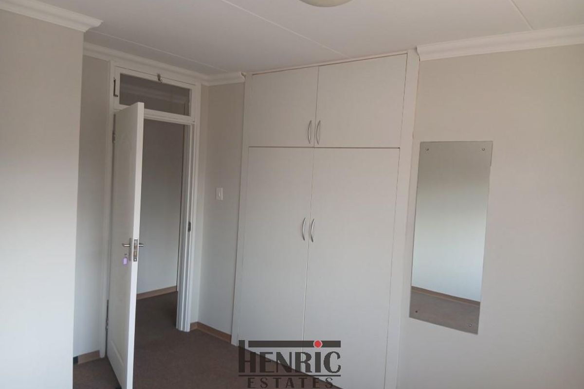 A clean, empty bedroom featuring built-in cupboards, neutral wall finishes, and carpeted flooring.