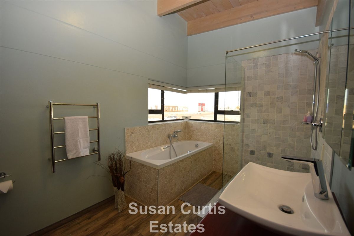 Modern bathroom featuring a built-in bathtub, glass-enclosed shower, vanity basin, and a heated towel rail with vaulted timber ceilings.