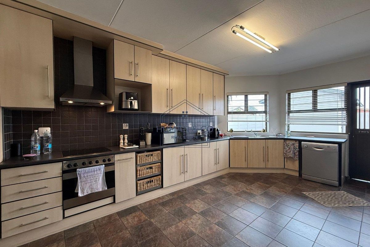 A functional kitchen featuring light wood cabinetry, dark tiled splashbacks, dark countertops, and tiled flooring with integrated oven and extractor fan.