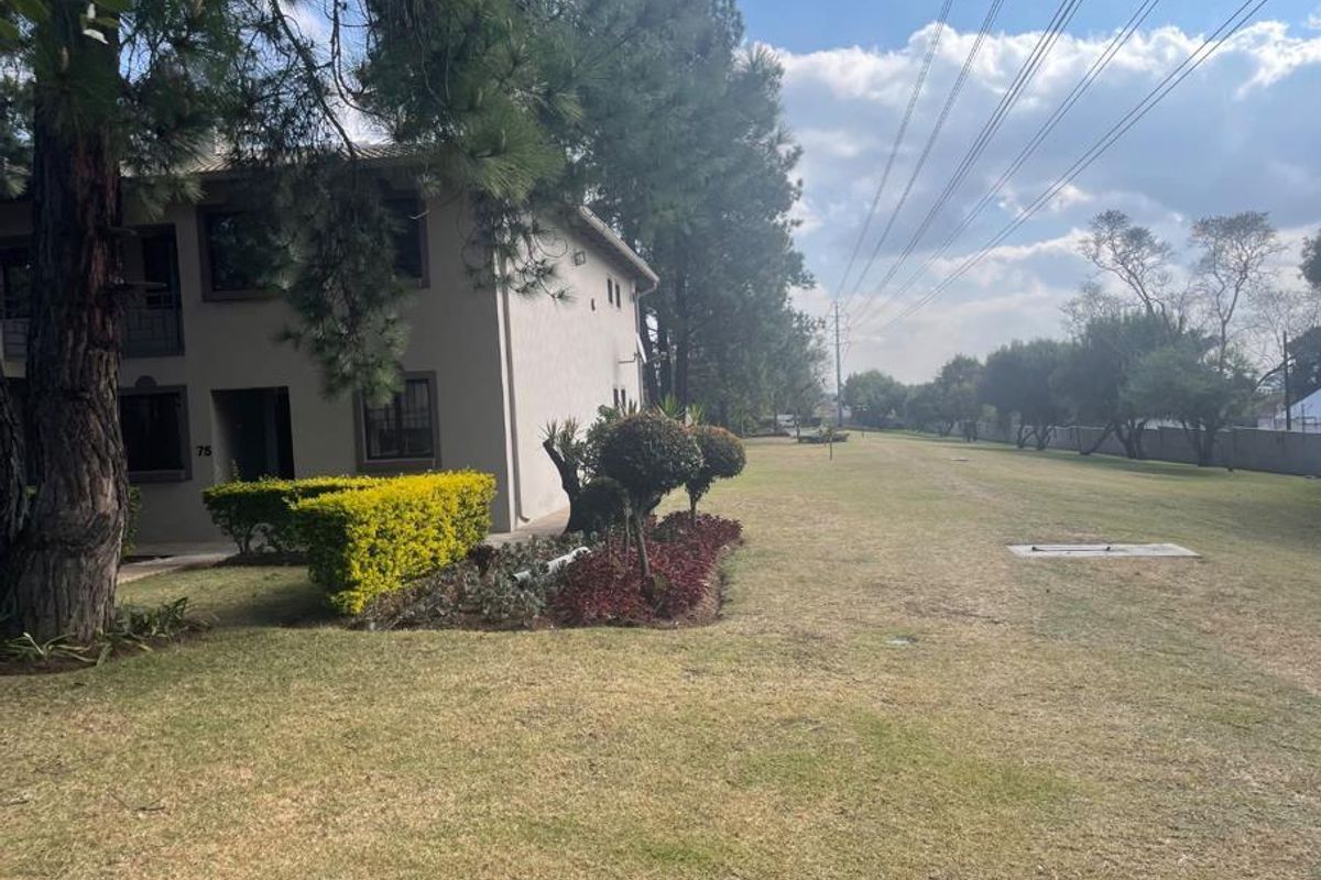 A view of the apartment building exterior featuring a well-maintained lawn and landscaped garden area.