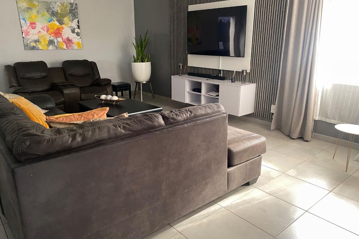 A comfortable living room featuring tiled flooring and a modern slatted feature wall with a mounted television setup.
