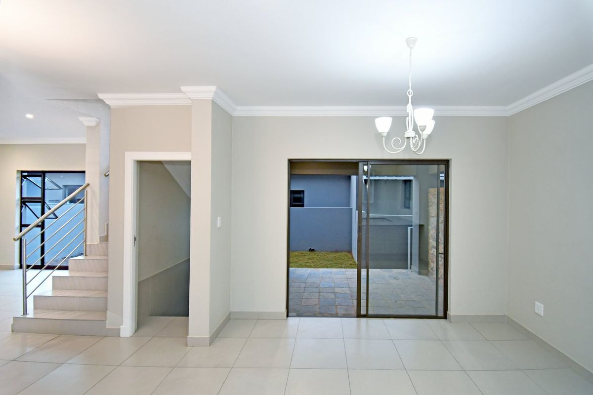 Spacious living area featuring neutral tiled flooring, crown molding, and a sliding glass door leading to an outdoor patio area.