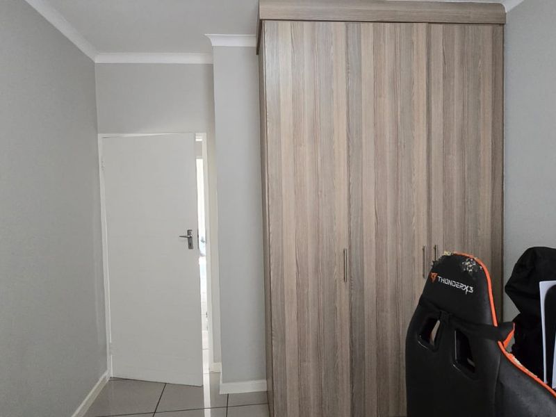 A bedroom featuring neutral grey walls, tiled flooring, and a modern wood-finish built-in wardrobe.