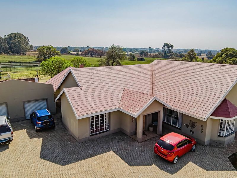 Aerial view of a residential small holding featuring a main dwelling with a tiled roof, paved driveway, and double garage set in a rural landscape.