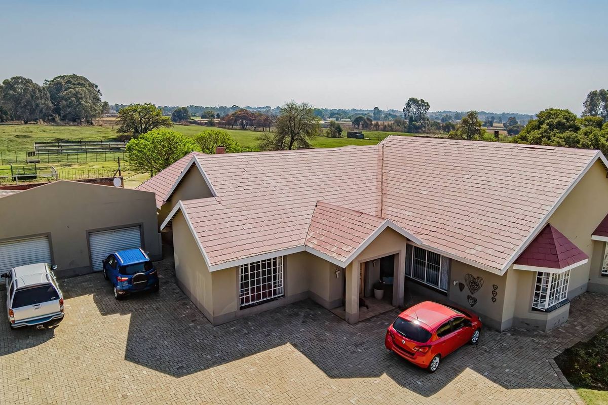Aerial view of a residential small holding featuring a main dwelling with a tiled roof, paved driveway, and double garage set in a rural landscape.