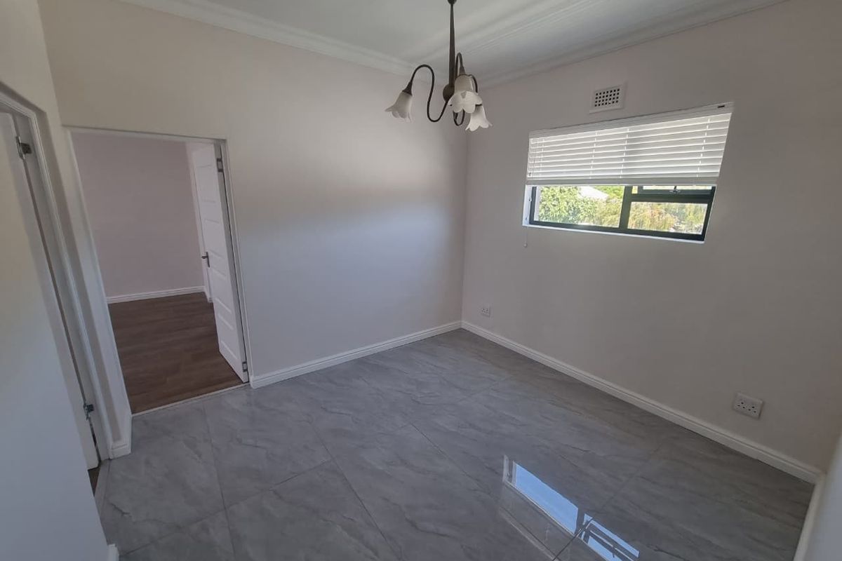 A bright, empty bedroom featuring modern grey porcelain floor tiles, neutral walls, and a classic ceiling light fixture.
