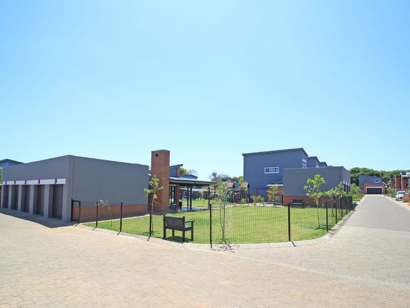 A view of the apartment complex exterior featuring a central communal garden area, paved driveway, and multiple garage units.