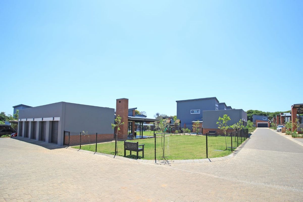 A view of the apartment complex exterior featuring a central communal garden area, paved driveway, and multiple garage units.