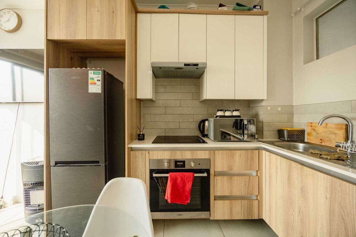 Modern kitchen featuring light wood-grain cabinetry, white upper cabinets, subway tile backsplash, integrated oven, hob, and extractor fan with a stainless steel sink.