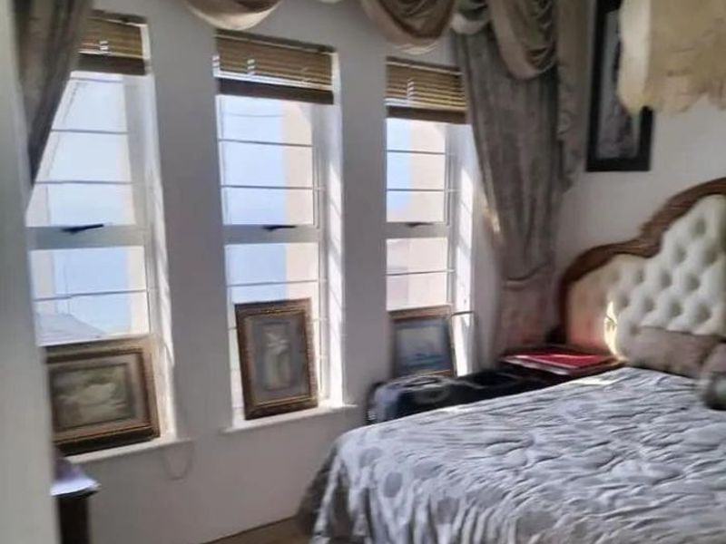 A bedroom featuring large windows with security bars, window blinds, and decorative curtain pelmets.