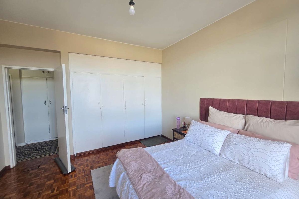 A bedroom featuring classic parquet flooring and built-in cupboards, offering a functional layout with direct access to an adjoining hallway.