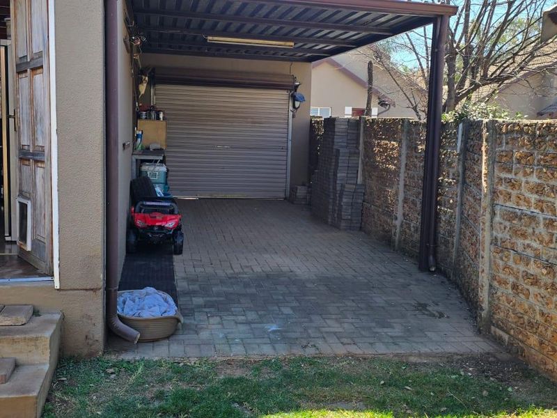 A covered carport area featuring a roller shutter garage door, paved flooring, and a stone boundary wall.