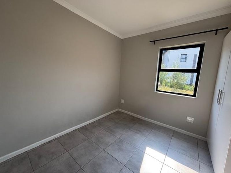 A clean, empty bedroom featuring neutral grey walls, tiled flooring, and a built-in wardrobe, offering a versatile space ready for personalization.