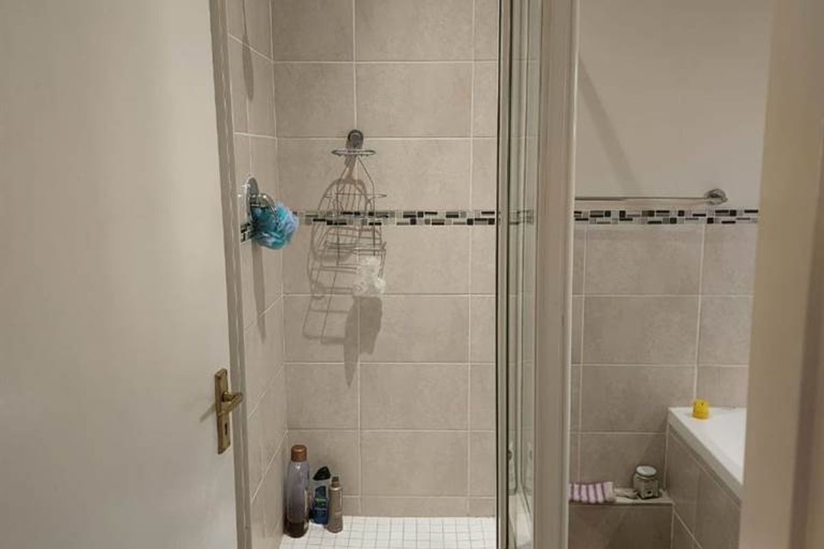 A functional bathroom featuring a tiled shower enclosure with a glass door and a separate bathtub with neutral wall tiling.