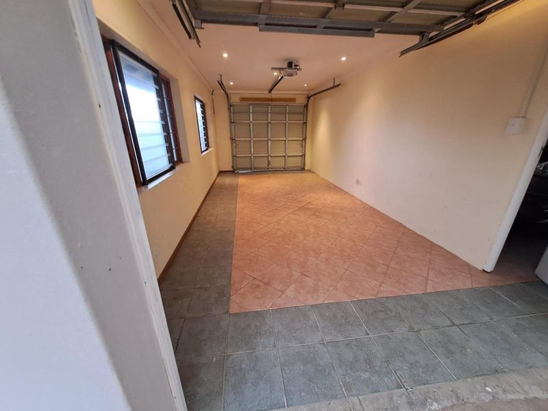 A clean, empty garage space featuring tiled flooring, louvered windows, and a functional sectional garage door with an automated motor.