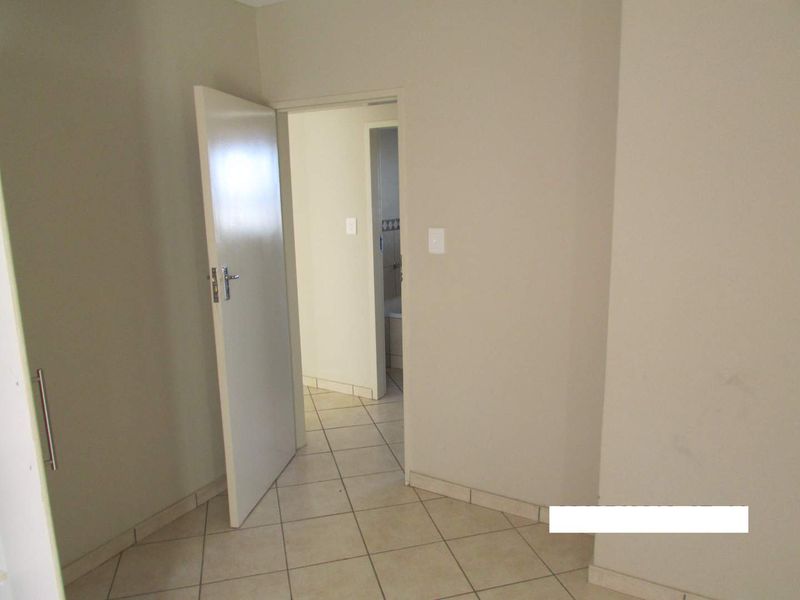 A neutral-toned hallway featuring tiled flooring and access to adjacent rooms, presenting a clean and functional transition space within the apartment.