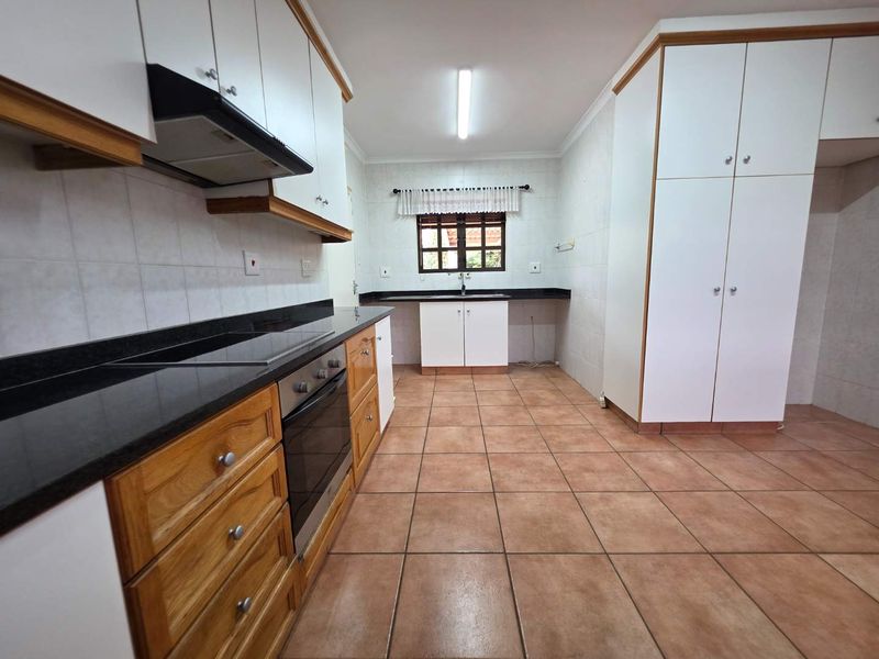 A spacious, empty kitchen featuring wooden and white cabinetry, granite countertops, built-in oven and hob, and tiled flooring throughout.