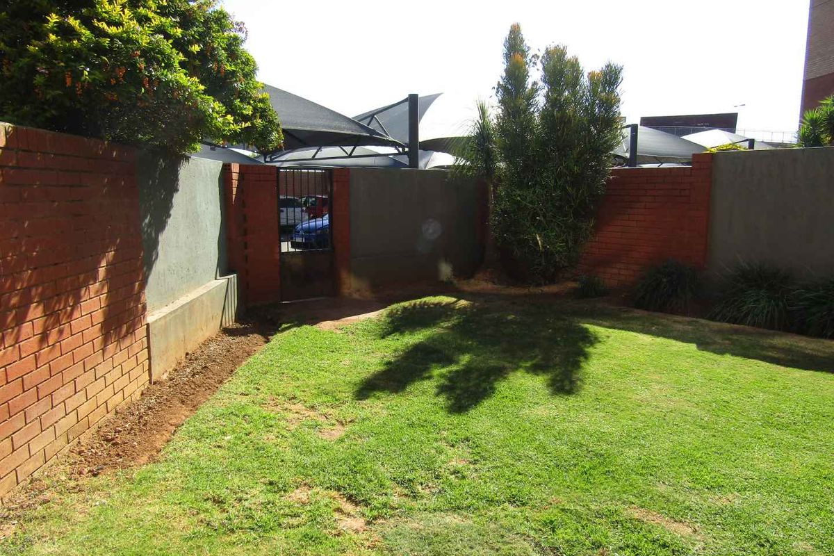 A private rear garden area featuring a lawn, enclosed by a combination of brick and rendered boundary walls with a metal access gate.