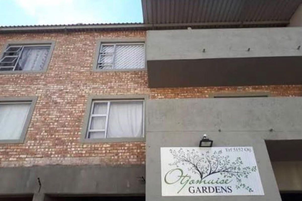Front facade of Otjomuise Gardens townhouse complex featuring face brick construction, concrete balconies, and aluminium window frames.
