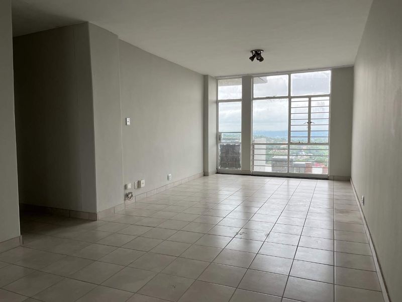 An empty, open-plan living area featuring neutral tiled flooring, large windows with security bars, and views of the surrounding area.