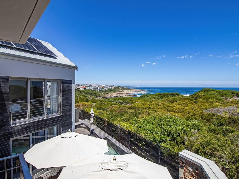 Elevated view of the coastal landscape and ocean, featuring a modern multi-level home with solar panels and a private deck area.