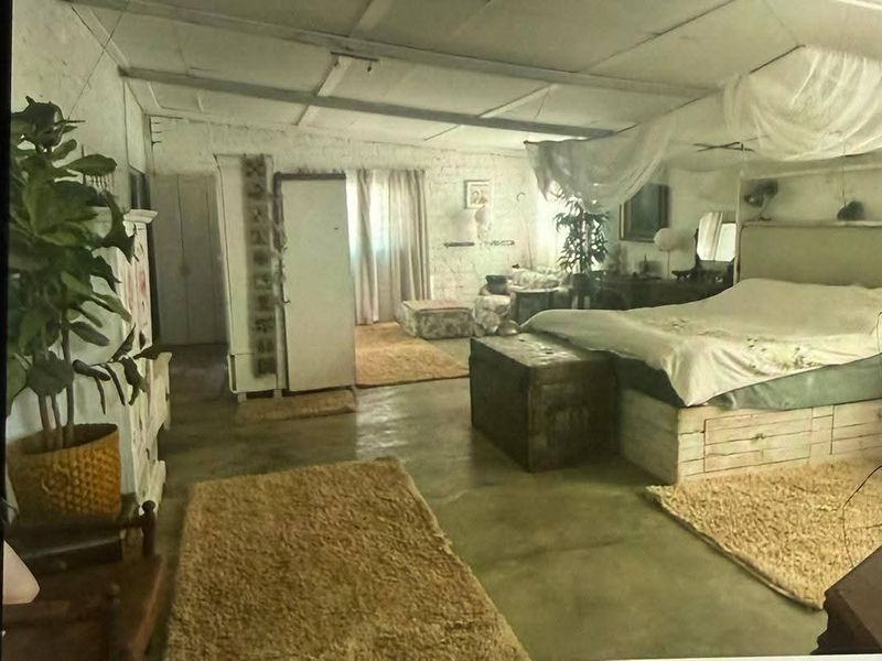 Spacious bedroom featuring rustic painted brick walls, exposed ceiling beams, and polished concrete flooring, offering a blank canvas for modern interior design updates.