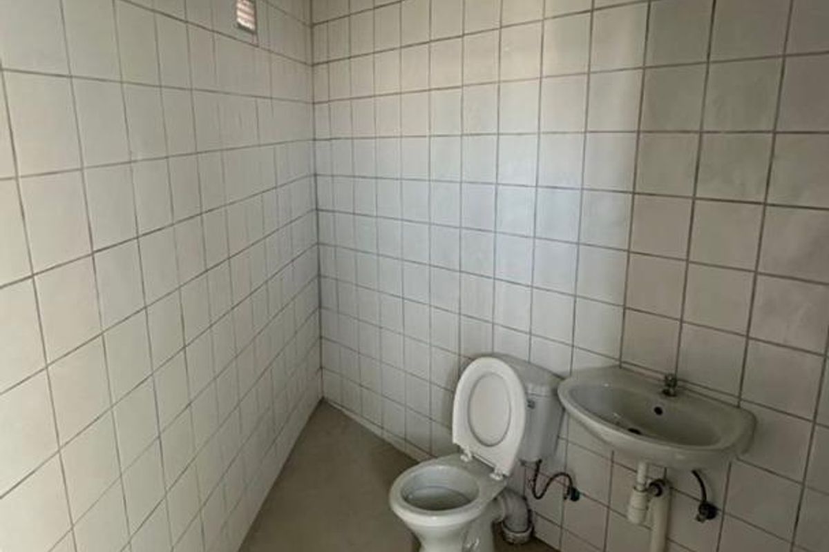 A small, dated office restroom featuring basic ceramic wall tiling, a standard toilet, and a wall-mounted basin.