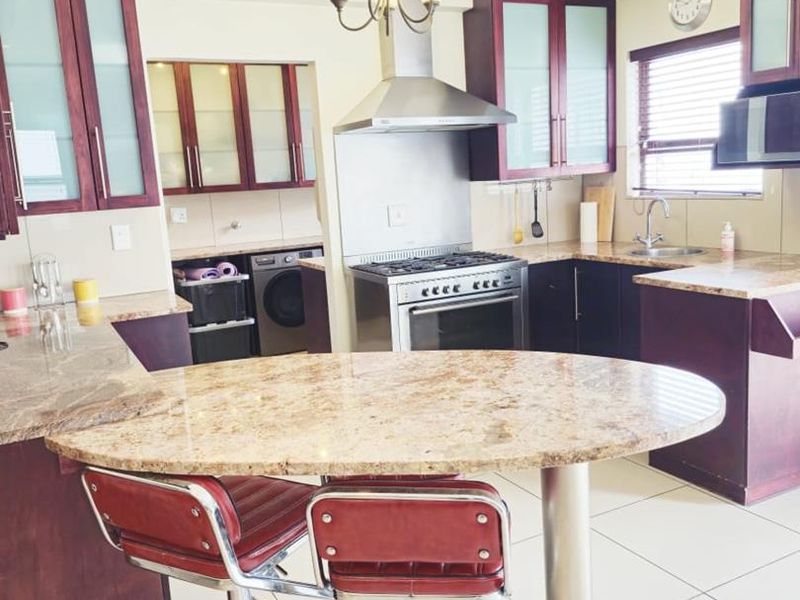 A functional kitchen featuring dark wood cabinetry, granite countertops, a breakfast bar, and stainless steel appliances, with an adjacent scullery area.
