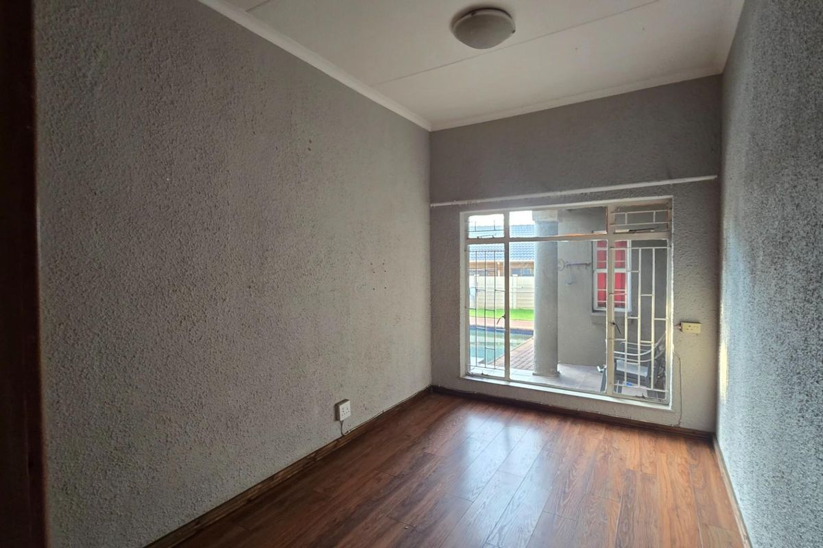 An empty bedroom featuring laminate flooring, textured walls, and a window fitted with security bars, offering a blank canvas for potential updates.
