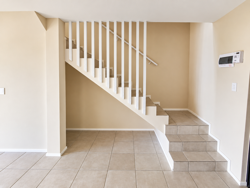 A clean, neutral-toned hallway featuring a tiled staircase with a white balustrade and a wall-mounted electrical distribution board.