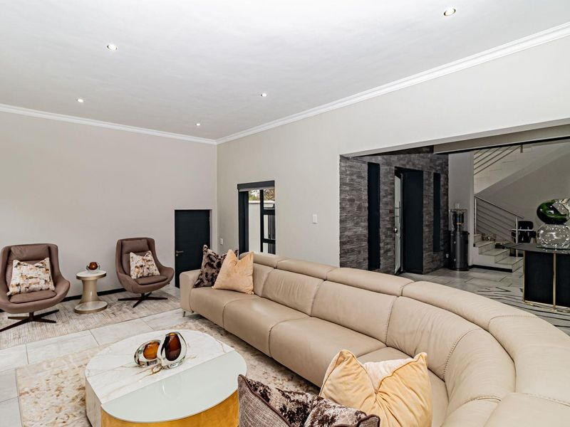 Spacious living room featuring tiled flooring, recessed downlighting, crown molding, and a decorative stone feature wall leading to an adjacent staircase area.