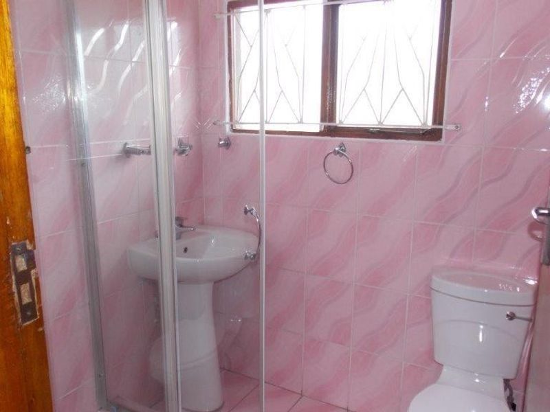 A compact bathroom featuring a pedestal basin, toilet, and a glass-enclosed shower, finished with dated pink wall tiles.