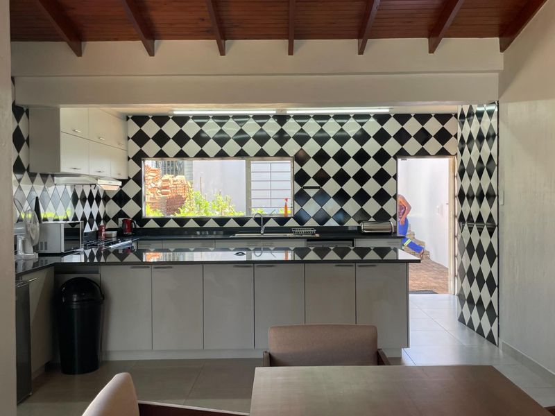 A well-lit kitchen featuring modern cabinetry, black granite countertops, and a distinctive checkerboard tiled backsplash under exposed timber ceiling beams.