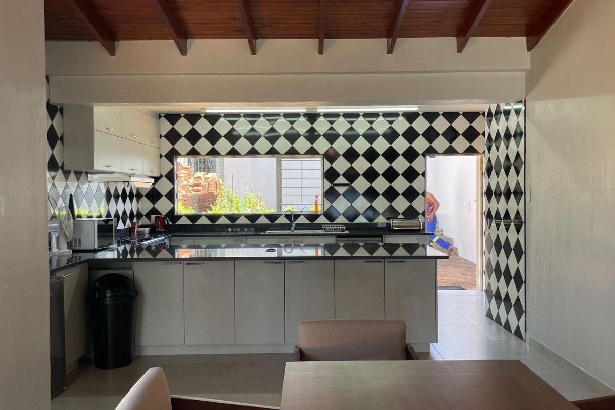 A well-lit kitchen featuring modern cabinetry, black granite countertops, and a distinctive checkerboard tiled backsplash under exposed timber ceiling beams.