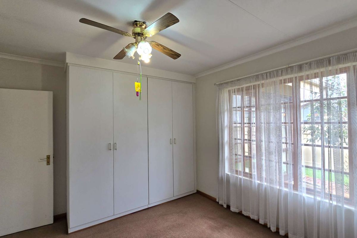 A bright, empty bedroom featuring built-in wardrobes, a ceiling fan, and large timber-framed windows overlooking the garden.
