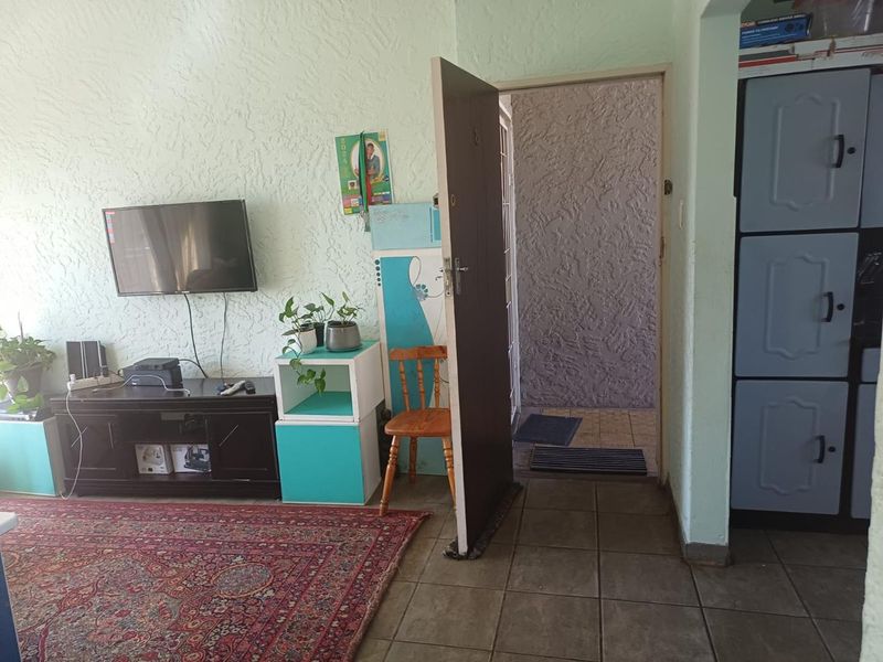 A living room area featuring tiled flooring, textured wall finishes, and a built-in storage cupboard, providing a functional and lived-in space.