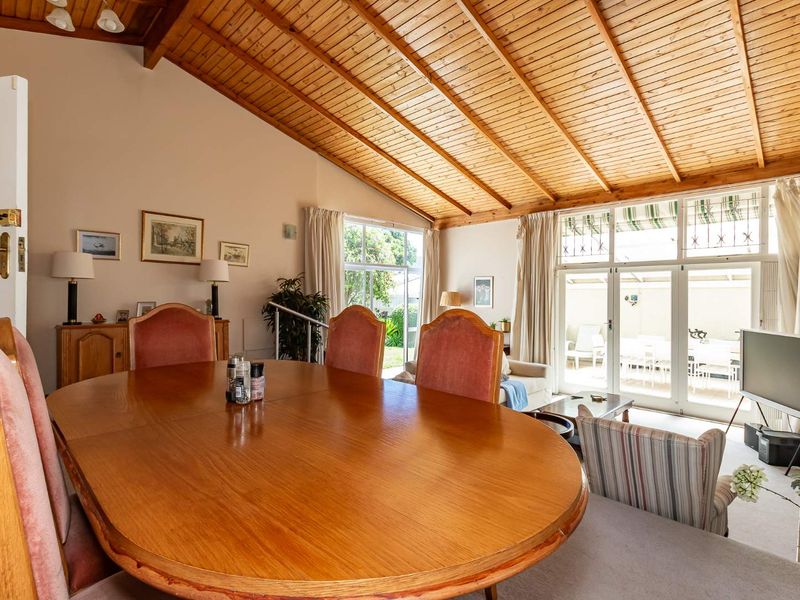 Spacious open-plan living and dining area featuring a high vaulted timber ceiling, exposed beams, and large glass doors leading to an outdoor patio.