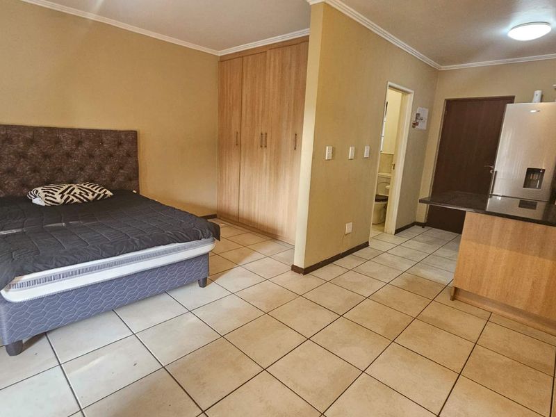 Open-plan studio apartment featuring tiled flooring, built-in bedroom cupboards, and a compact kitchen area with granite countertops.